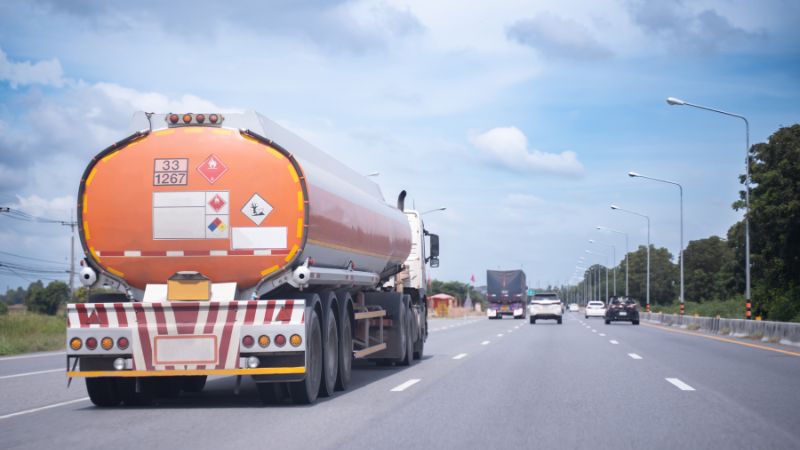 Fuel tanker truck on highway with safety hazard signage and clear sky.
