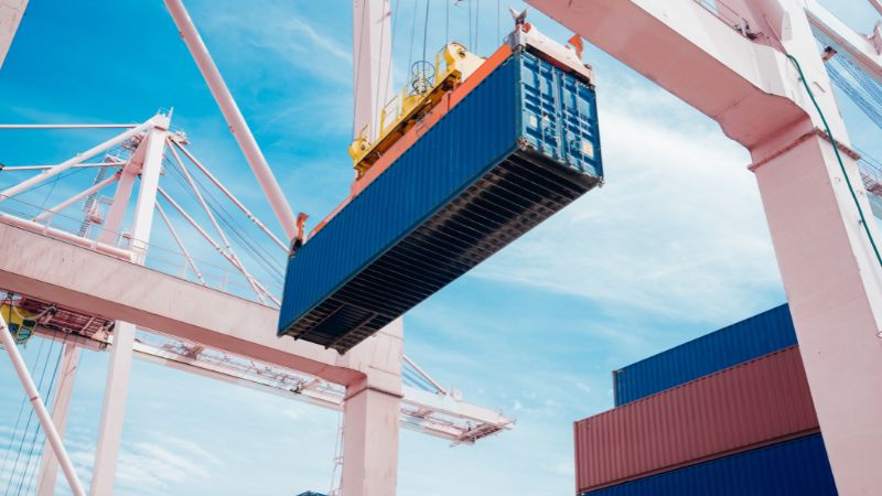 High-resolution cargo container being lifted by port crane at shipping yard, emphasizing logistics and maritime transportation.