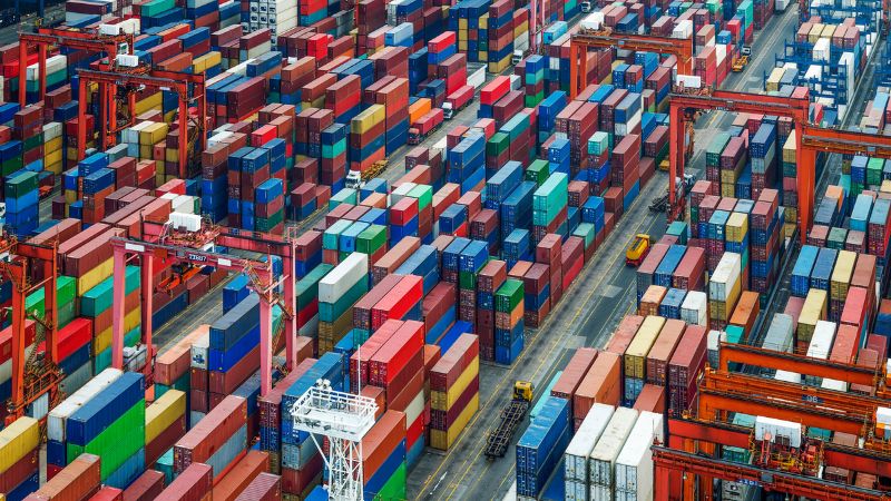 Aerial view of a busy shipping yard with stacked colorful cargo containers and active cranes.