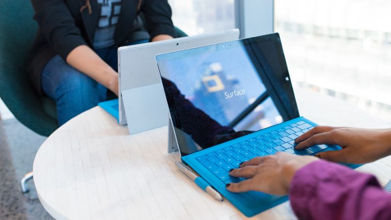 Two people working at a table on Microsoft Surface tablets with blue keyboards.